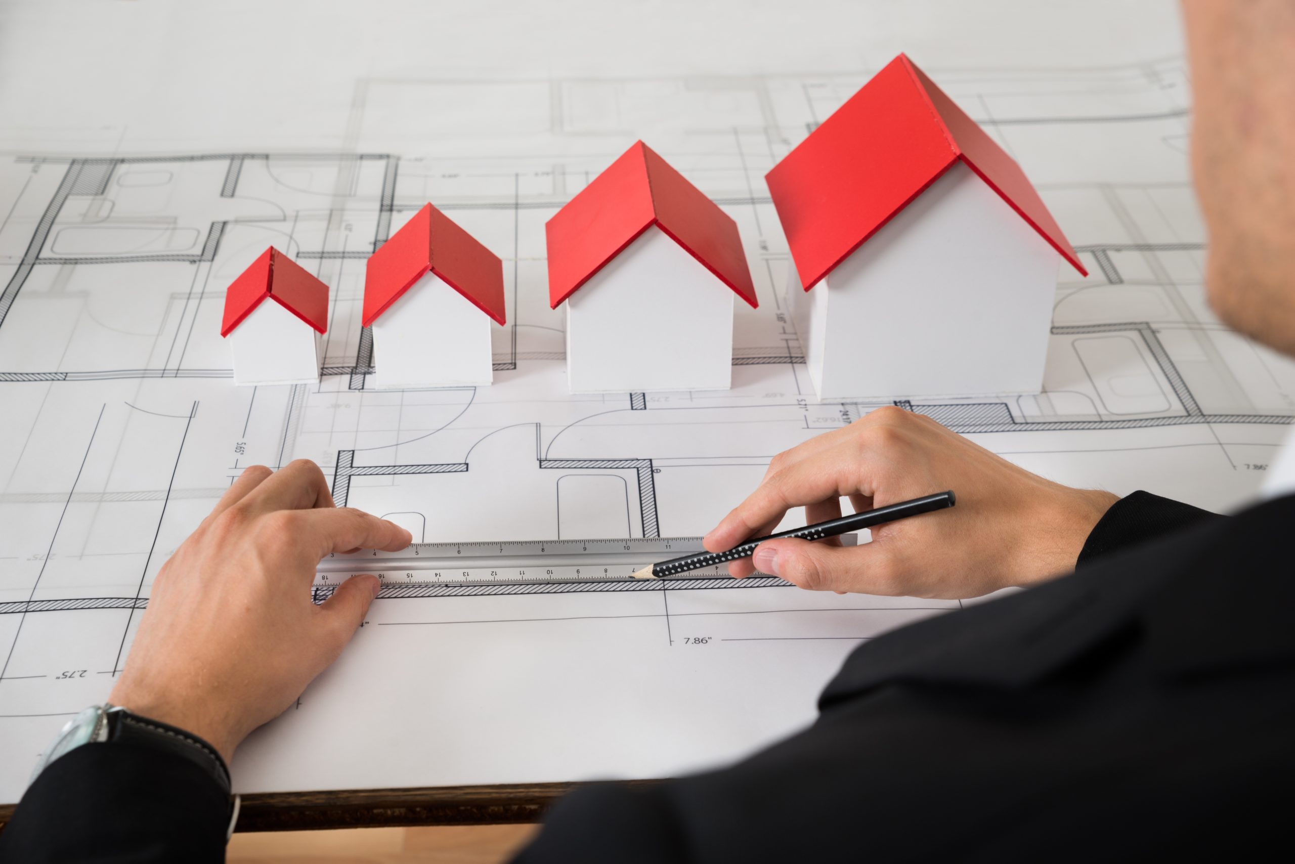 Close-up Of Architect With Different Size House Models On Blueprint In Office