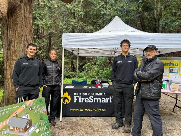 Four members of the SCRD FireSmart team stand in front of a table and tent.