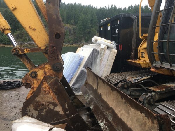 A construction vehicle loads garbage onto a barge. 